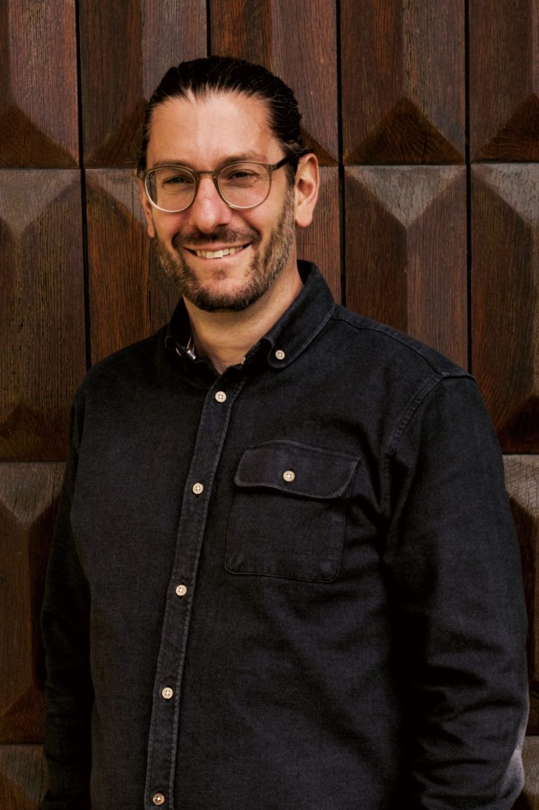 Matthias Kortmann vor einer holzverzierten Wand, lächelnd.